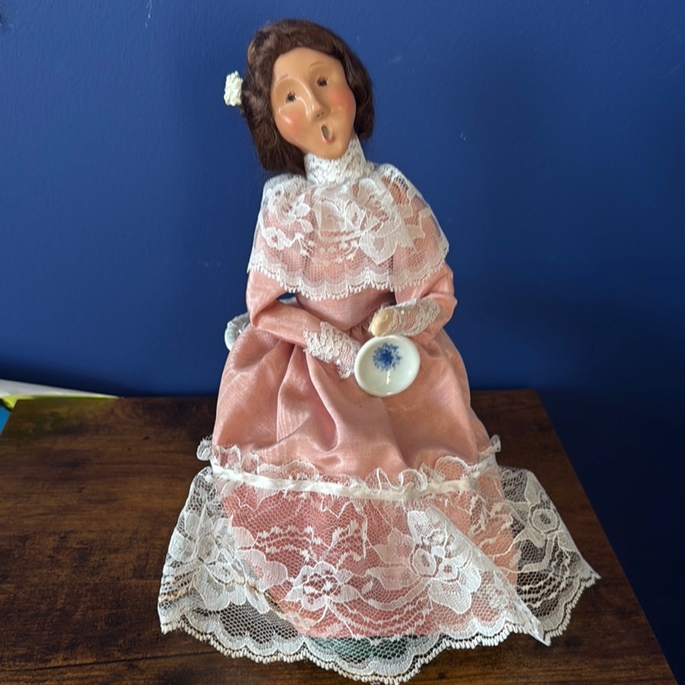 Byer’s Choice Lady in Pink Lace Dress sitting in white whicker chair.